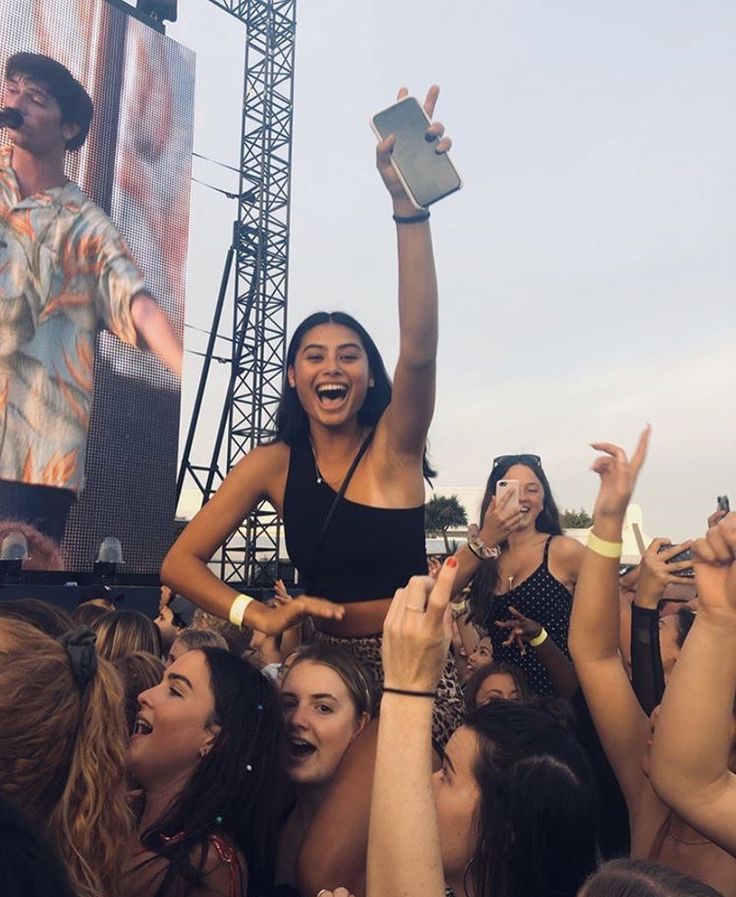 a woman standing on top of a crowd of people holding up their hands in the air