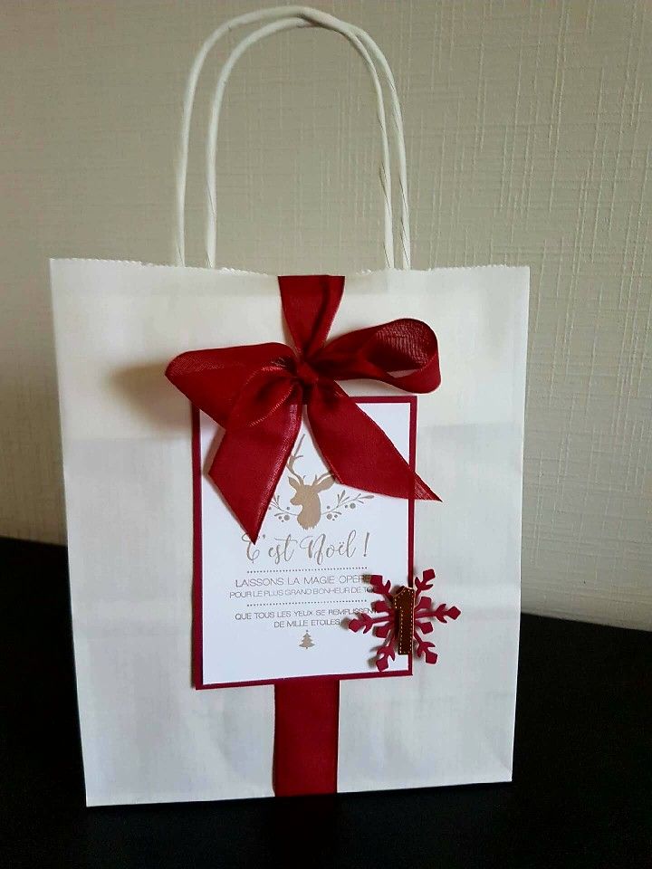 a white paper bag with a red ribbon on it and a card attached to the front