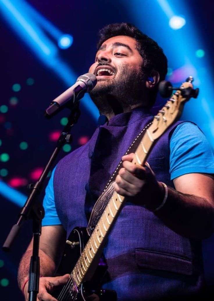 a man singing into a microphone and holding a guitar in his hand while standing on stage