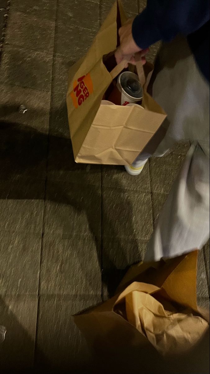 a person holding a can and some brown paper bags on the ground with food in them