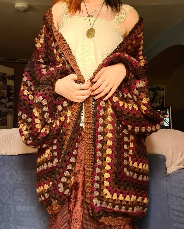 a woman standing in front of a couch wearing a crocheted shawl