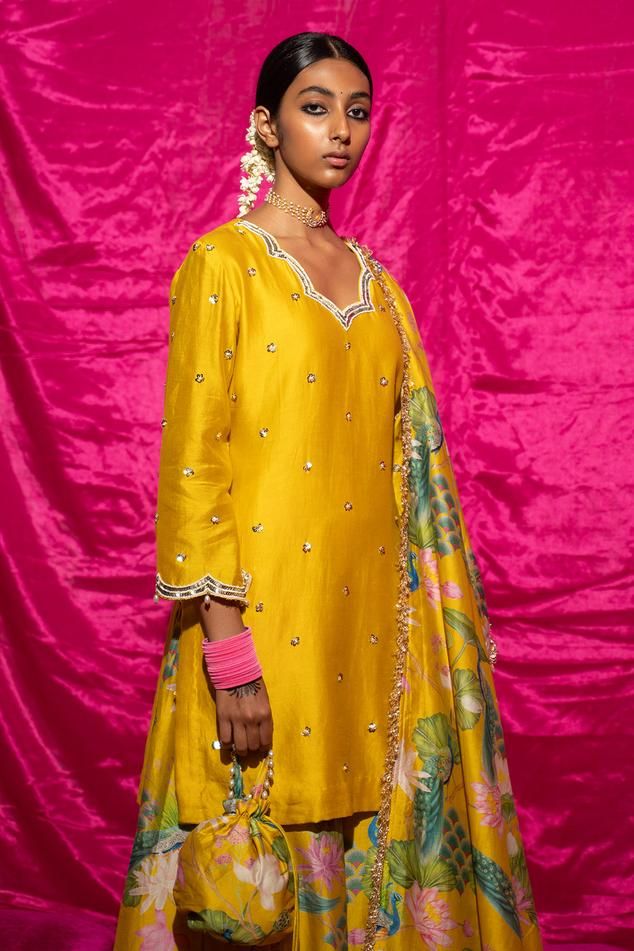 Yellow chanderi silk kurta with sequin, pearl placement embroidery. Paired with floral print sharara and fringe bordered dupatta.
Components: 3
Pattern: Printed, Embroidery
Type Of Work: Floral, sequin, pearl
Neckline: Scallop V neck
Sleeve Type: Long sleeves
Fabric: Chanderi Silk, Lining: Shantoon
Color: Yellow
Other Details: 
Fringe tassel bordered dupatta
Length:
Kurta: 35 inches
Sharara: 38 inches
Note: Potli shown in the image is not for sale
Occasion: Sangeet - Aza Fashions Floral Print Sharara, Placement Embroidery, Printed Embroidery, Kurta Set For Women, Silk Kurta, Tassel Fringe, Kurta Set, Set For Women, Aza Fashion