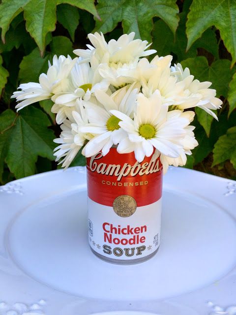 a can filled with white flowers sitting on top of a table next to green leaves