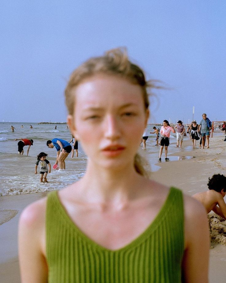 a woman standing on top of a sandy beach next to the ocean with lots of people in the background