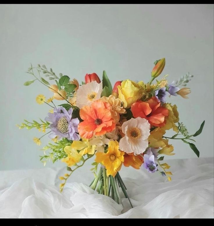 a vase filled with lots of colorful flowers on top of a white bed cover covered in sheets