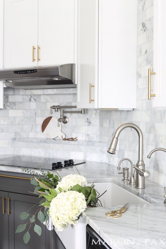 a white kitchen with marble counter tops and gold trimmings on the backsplash