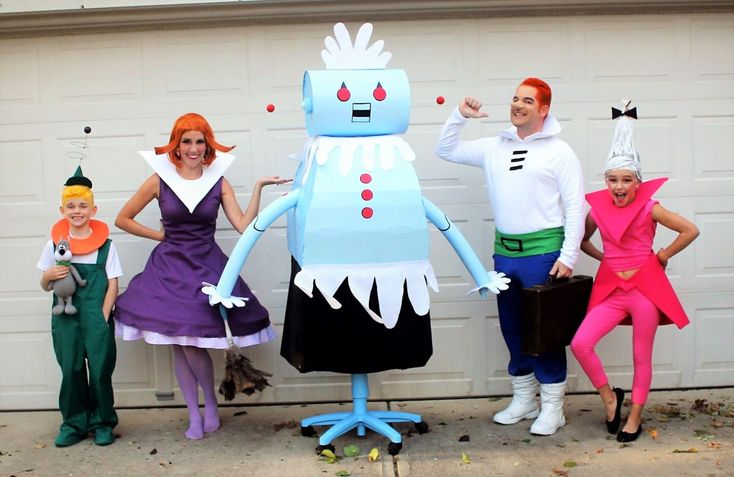 four people dressed up in costumes standing next to a garage door with a robot on it