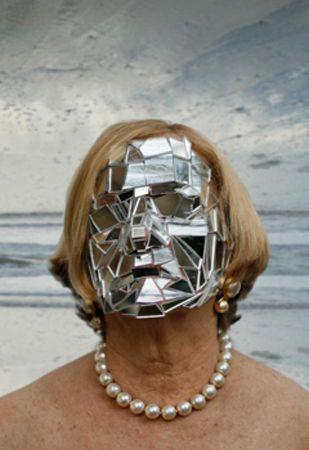 a woman wearing a silver mask with pearls around her neck and necklace in front of the ocean