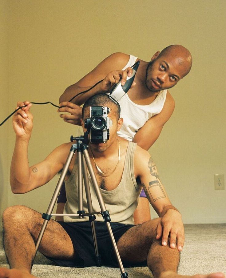 a man sitting on the floor with a camera in front of him and another man standing behind him