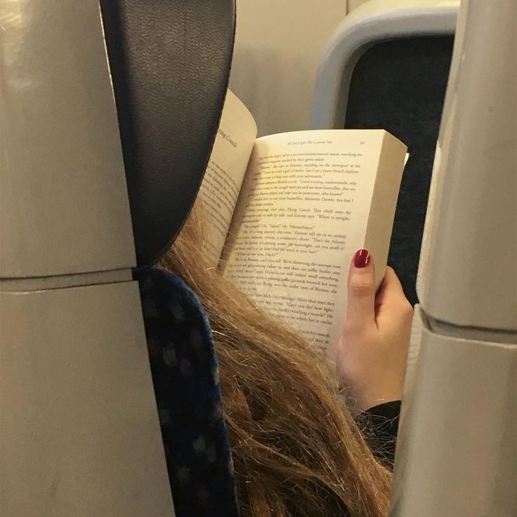 a woman is reading a book while sitting on an airplane with her head turned to the side