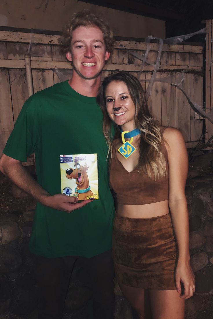 a man and woman standing next to each other in front of a wooden fence holding a book