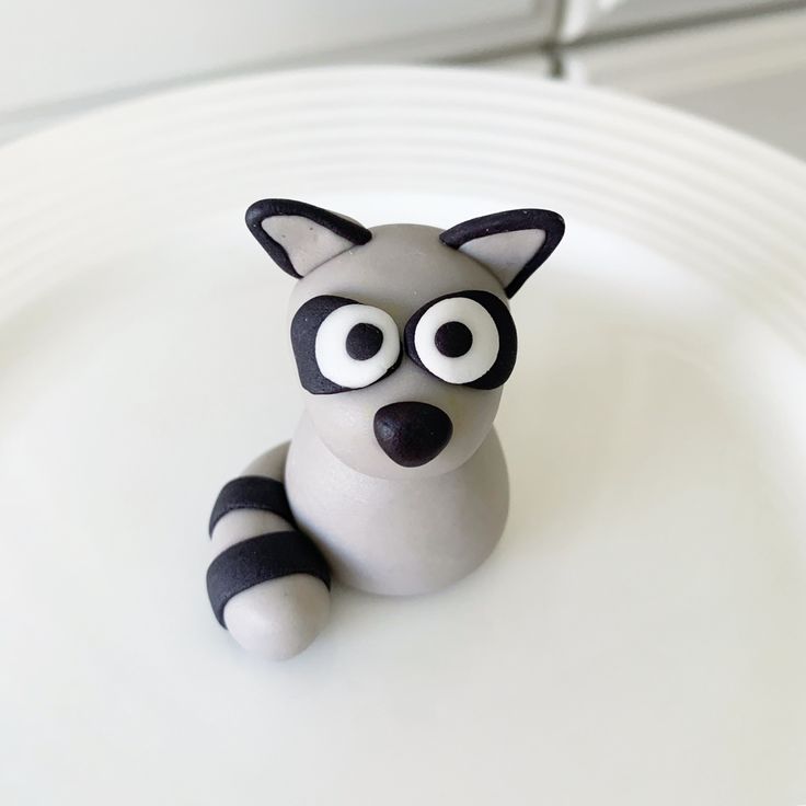 a small toy racoon sitting on top of a white plate with eyes painted on it