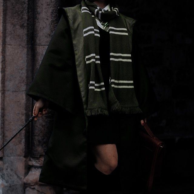 a woman in black and white striped scarf holding a brown bag while standing next to a stone wall