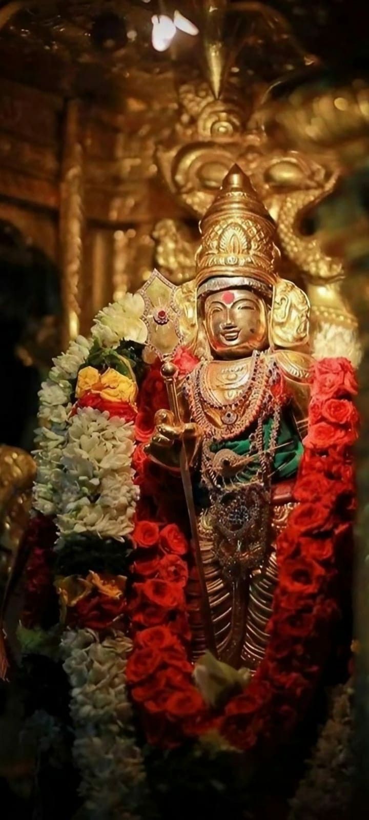 the statue is adorned with red and white flowers in front of a golden wall behind it