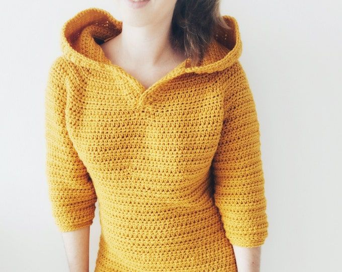 a woman is wearing a yellow sweater and smiling at the camera while standing in front of a white wall