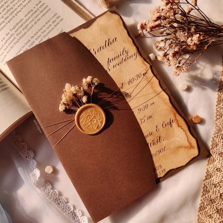 an open book with a wax stamp on it sitting next to some flowers and lace