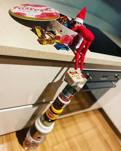 an elf on top of a kitchen counter with candy in the bottom drawer and other items around it