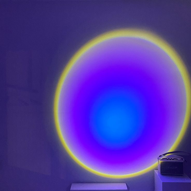 a blue and purple circular light in a white room with a printer on the floor