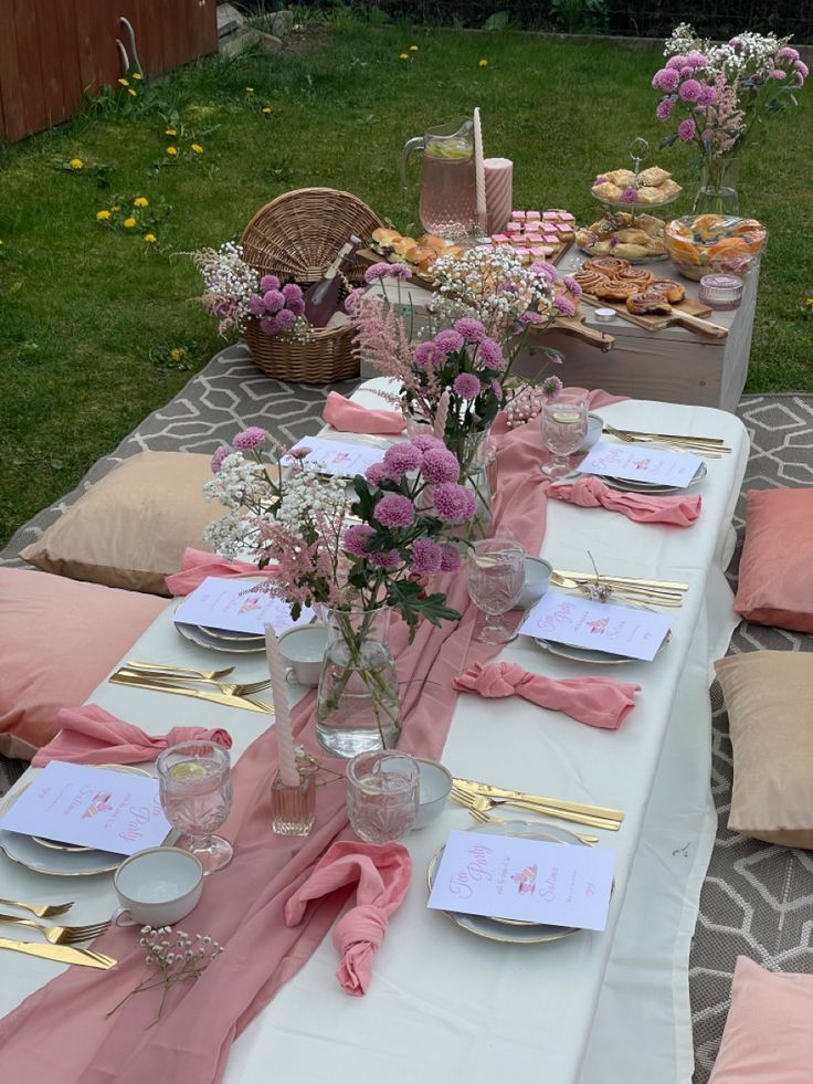 a table set up with pink napkins and place settings for an outdoor dinner party