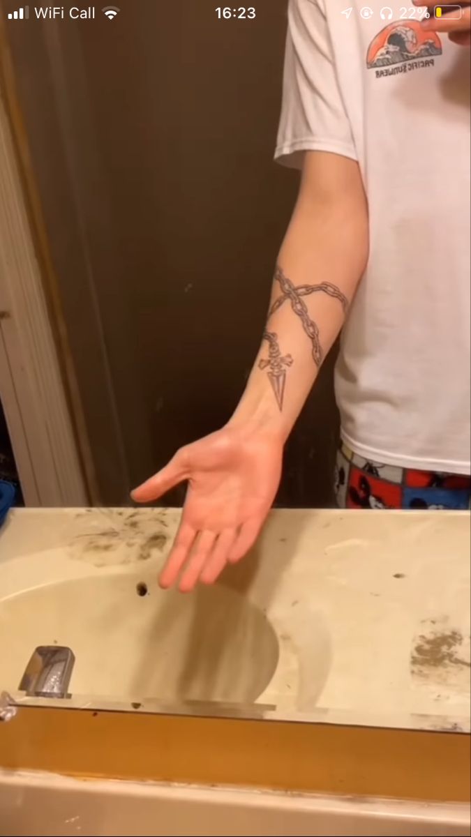 a man with a cross tattoo on his arm reaching for the sink in front of him