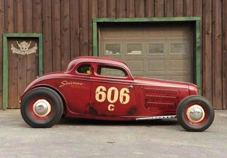 an old red car parked in front of a garage