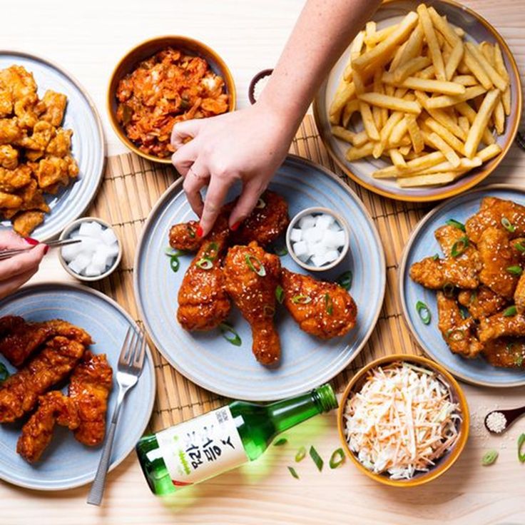 several plates of food on a table with people reaching for some chicken wings and french fries