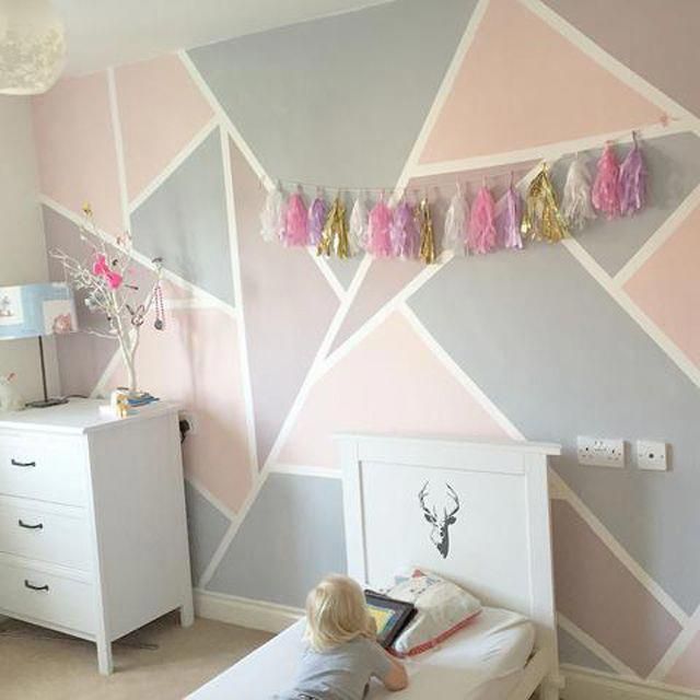 a child is sitting on a bed in a room with pink, grey and white walls