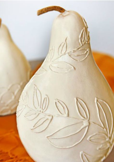 two white ceramic pears sitting on top of an orange cloth covered table with leaves