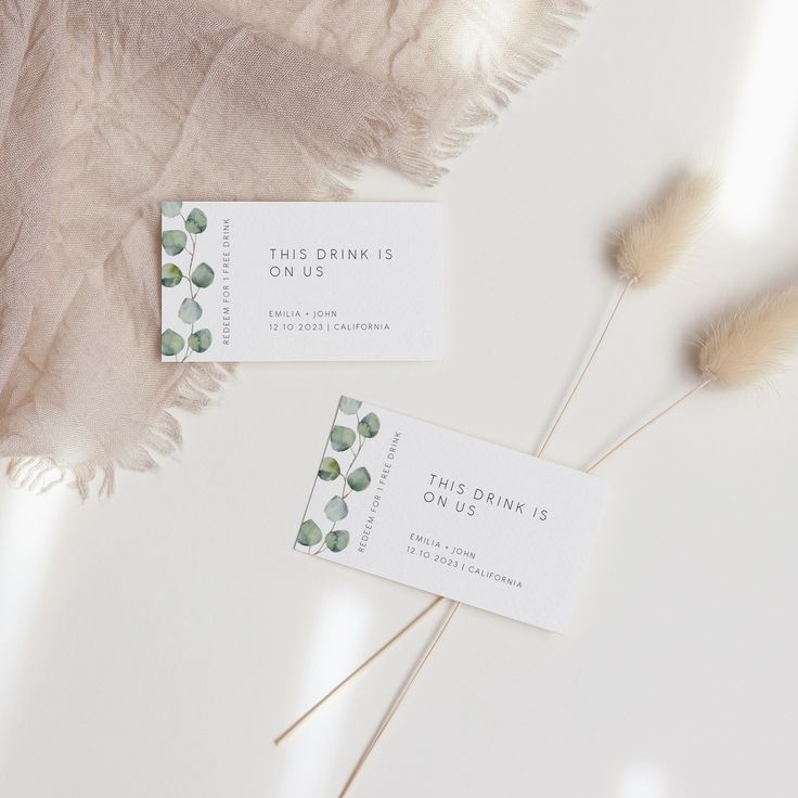 two business cards sitting next to each other on top of a white table with feathers