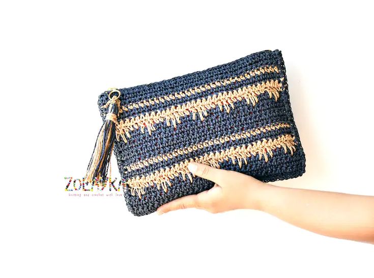 a hand holding a crocheted blue and white purse with tassels on it