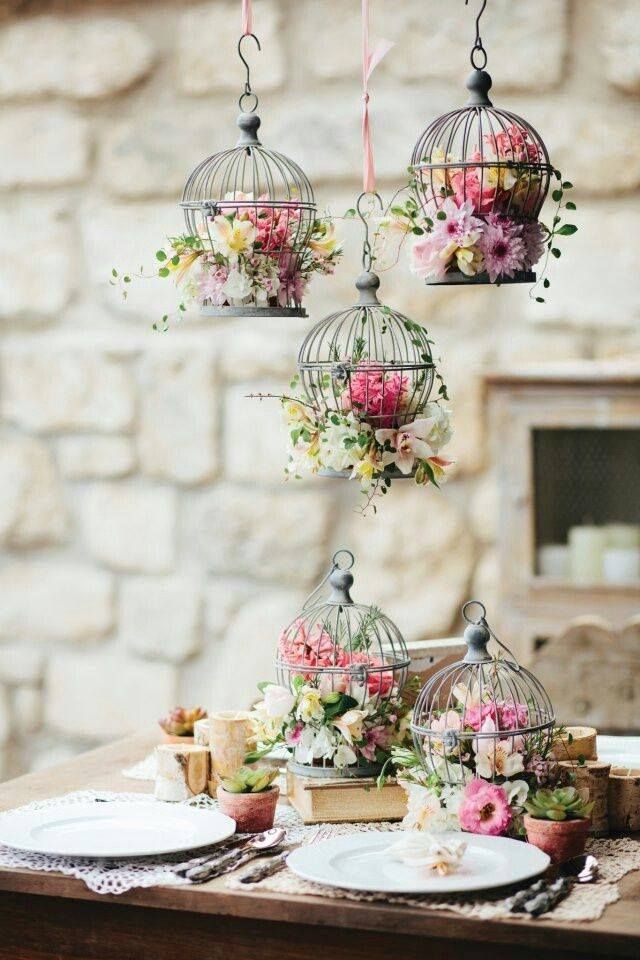 a table topped with plates and flowers next to a birdcage filled with flowers