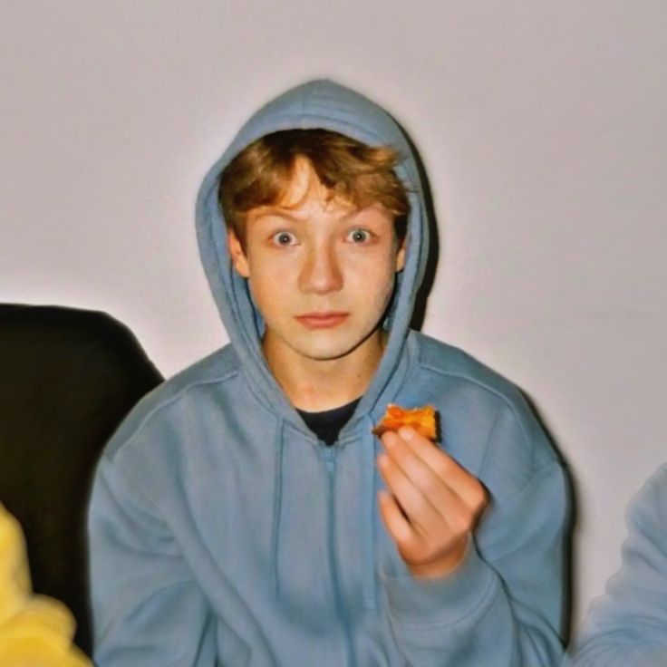 a young man in a blue hoodie eating pizza