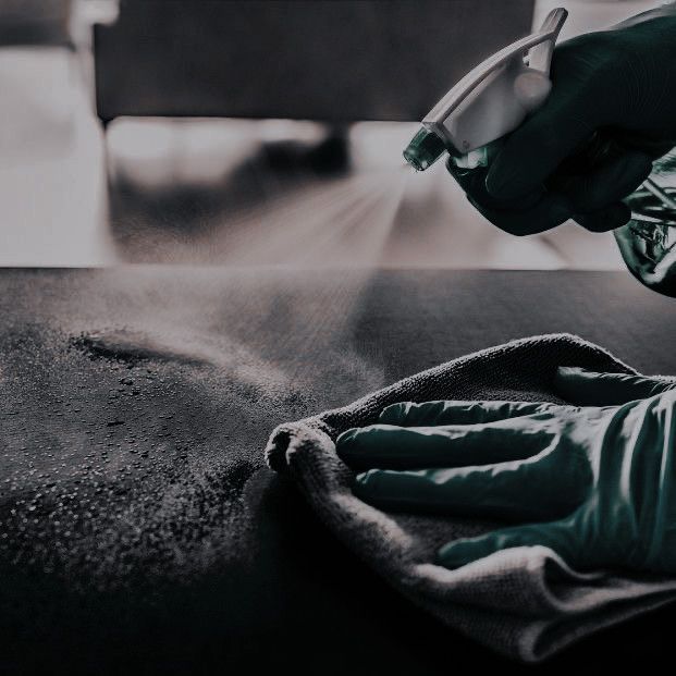 a gloved hand is cleaning a table with a spray bottle and cloth on it