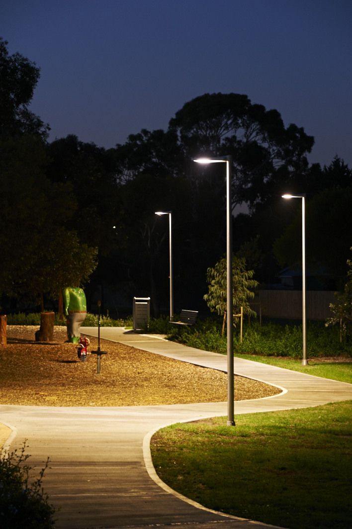 a person walking down a path at night with street lights on the side and trees in the background