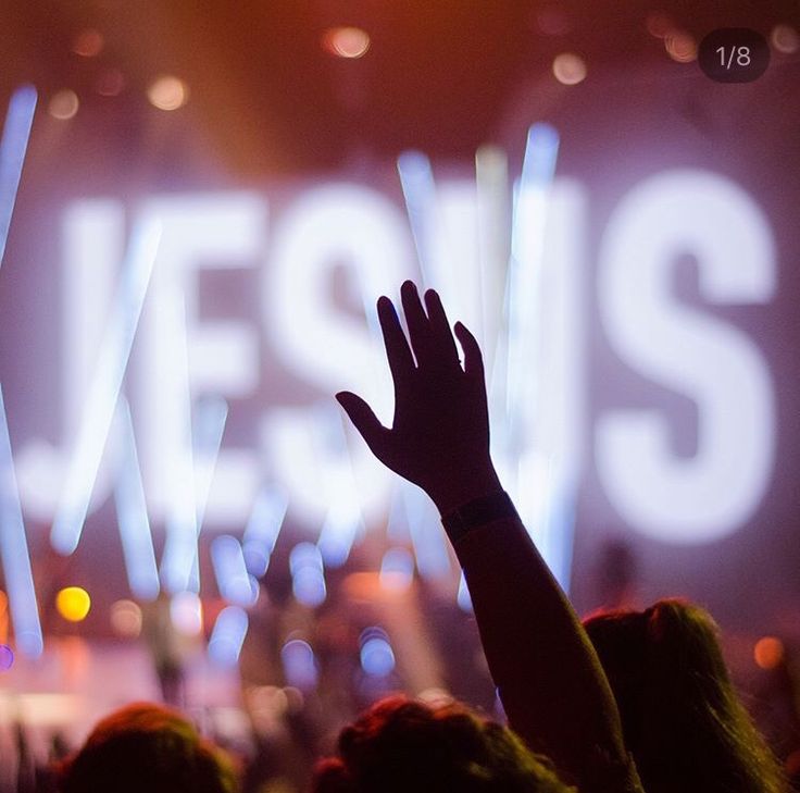 a person raising their hand up in front of a stage with the word jesus on it