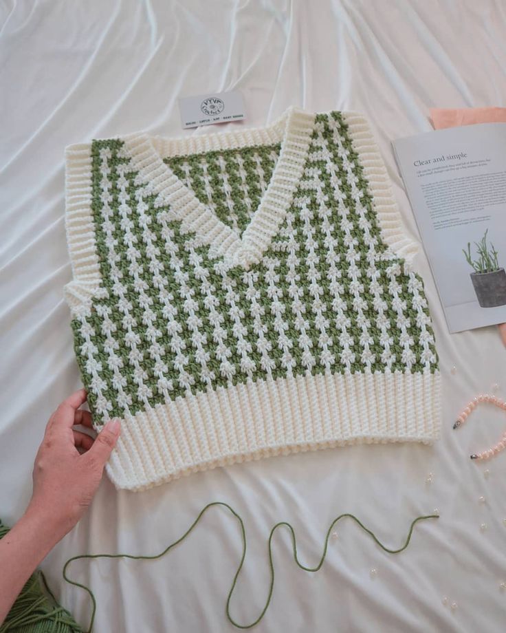 a green and white sweater sitting on top of a bed next to a knitting kit