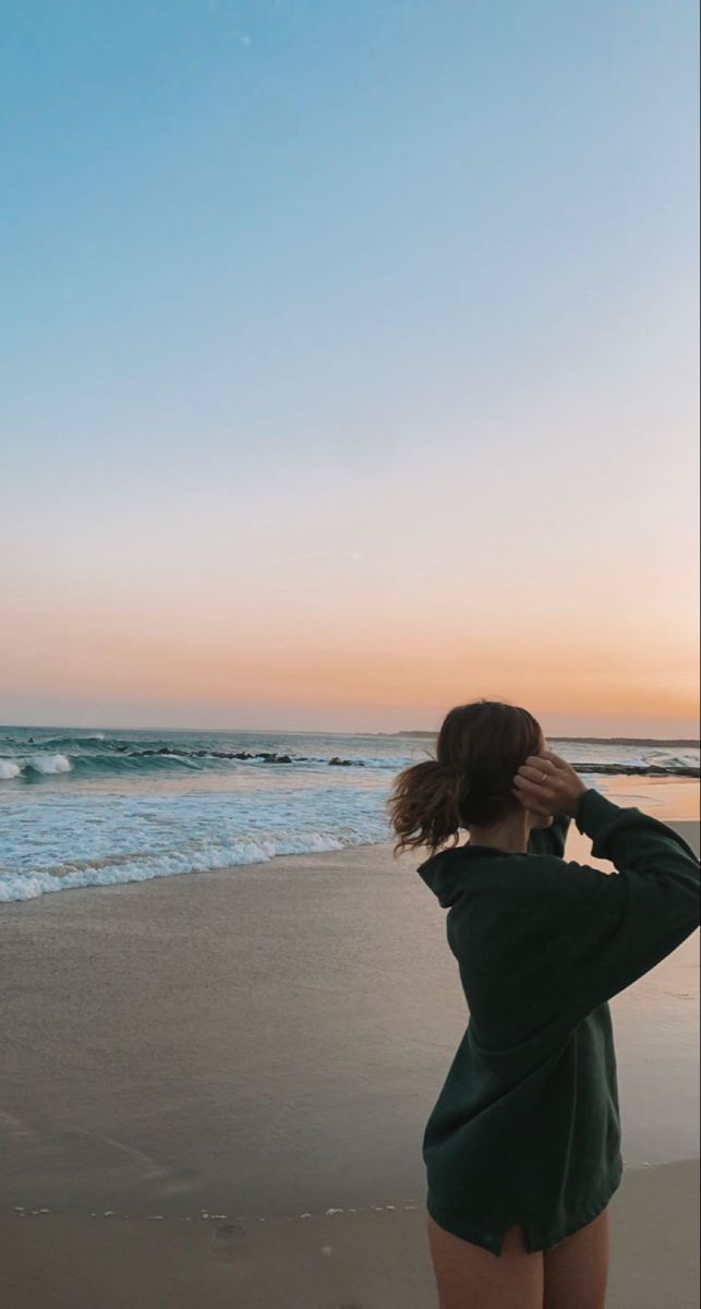 a woman standing on top of a sandy beach next to the ocean at sundown