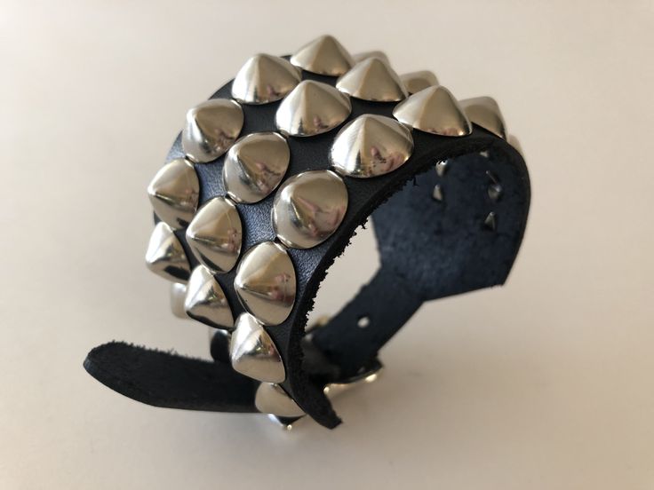 "Black leather studded punk bracelet with 3 rows of cone studs. Cone studs are 1/2\" wide and about 3/8\" tall so bracelet can easily be worn under jacket sleeves. Cone studs are made from high quality nickel plated brass. Buckle and rivets are also nickel plated. Bracelet is 1.75\" wide. Smaller cuff has fewer studs. Made out of hand dyed vegetable tan leather. Ask about custom sizes and colors!" Punk Leather Bracelet With Studs For Festivals, Punk Style Studded Leather Bracelet For Festivals, Gothic Leather Bracelet With Spikes For Party, Metal Leather Bracelet With Rivets For Festival, Punk Leather Jewelry With Rivets, Adjustable Metal Bracelets With Studs, Rock Style Spiked Jewelry For Parties, Rock Style Party Jewelry With Spikes, Rock Style Spiked Party Jewelry