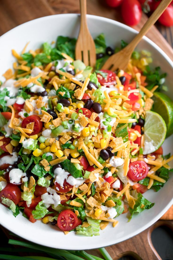 a salad in a white bowl topped with corn, tomatoes, black olives and lettuce