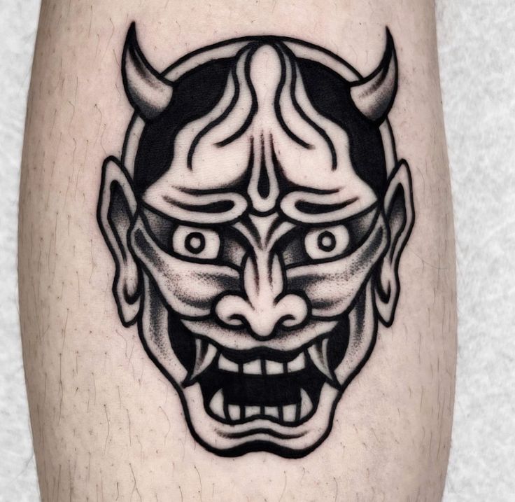 a black and white image of a demon mask on the leg, with an evil look