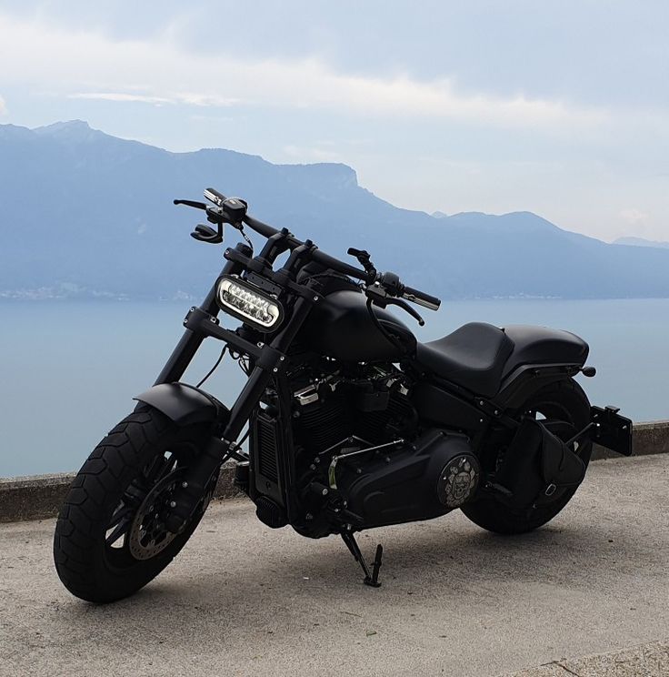 a black motorcycle parked on the side of a road next to some water and mountains