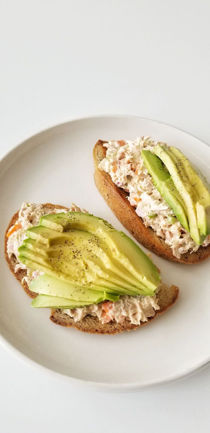 an open faced sandwich with avocado and chicken salad on it sitting on a white plate