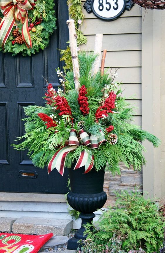 a black vase filled with red and white flowers sitting in front of a door decorated for christmas