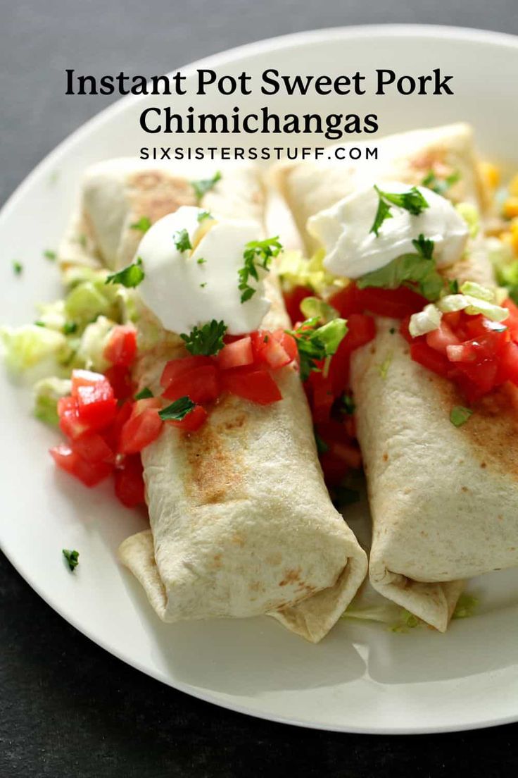 two burritos on a white plate topped with tomatoes, lettuce and sour cream