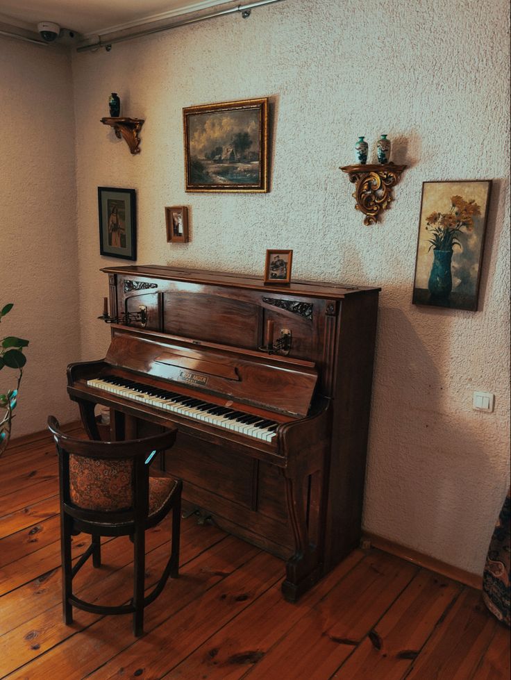 an old piano sits in the corner of a room with wood floors and paintings on the wall