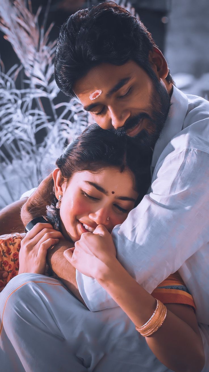 a man and woman embracing each other in front of plants