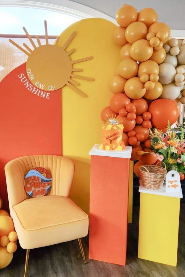 an orange chair sitting in front of a wall with balloons on it and a sun shaped balloon