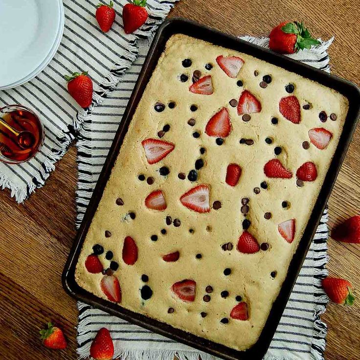 a cake with strawberries and chocolate chips on it sitting on a table next to a plate