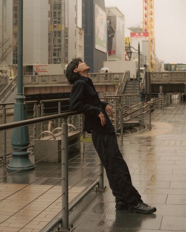 a man leaning on a rail in the rain with his eyes closed while looking up