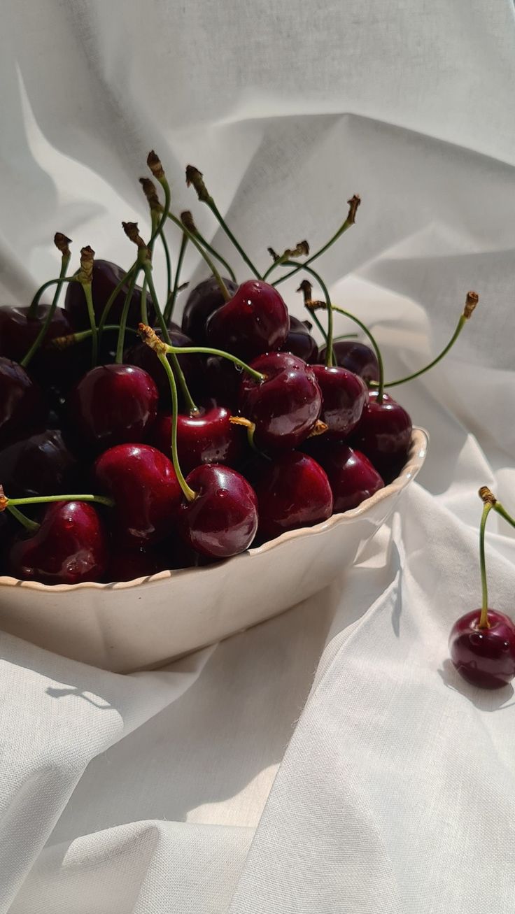 a bowl filled with cherries on top of a white cloth